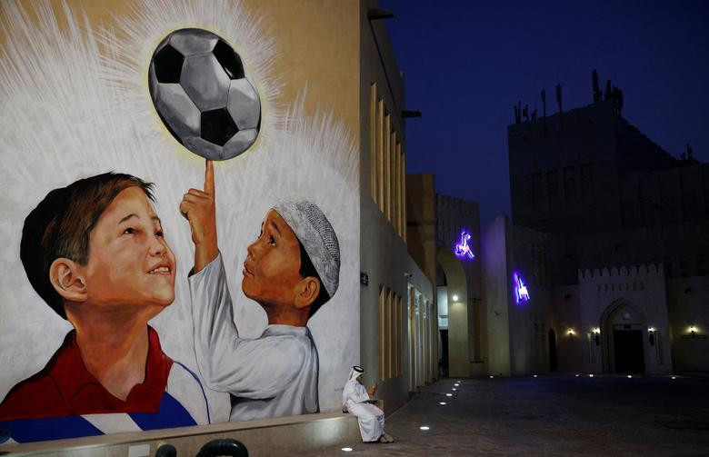 Một người đàn ông ngồi bên bức tranh tường bóng đá trên tường của Làng văn hóa Katara trước thềm World Cup, Doha, Qatar.