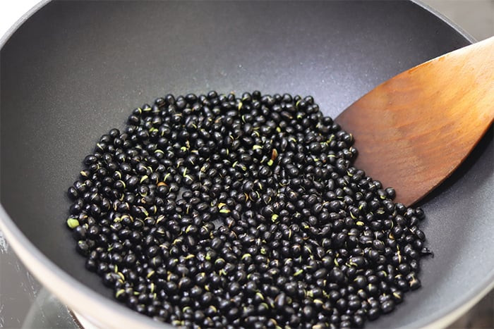 Bắt đầu làm giấm ngâm đậu đen Đậu đen rang trên lửa nhỏ tới khi tách vỏ, có mùi thơm. (Ảnh: Sohu)