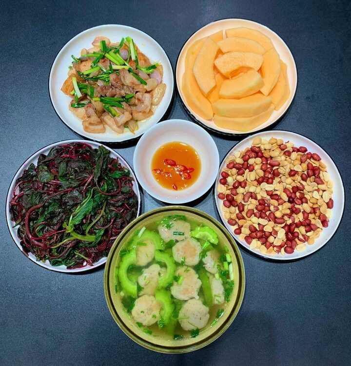 Mâm cơm đơn giản với thịt rang, lạc rang, canh mướp đắng nấu chả cá thác lác, rau dền luộc và tráng miệng với dưa vàng.