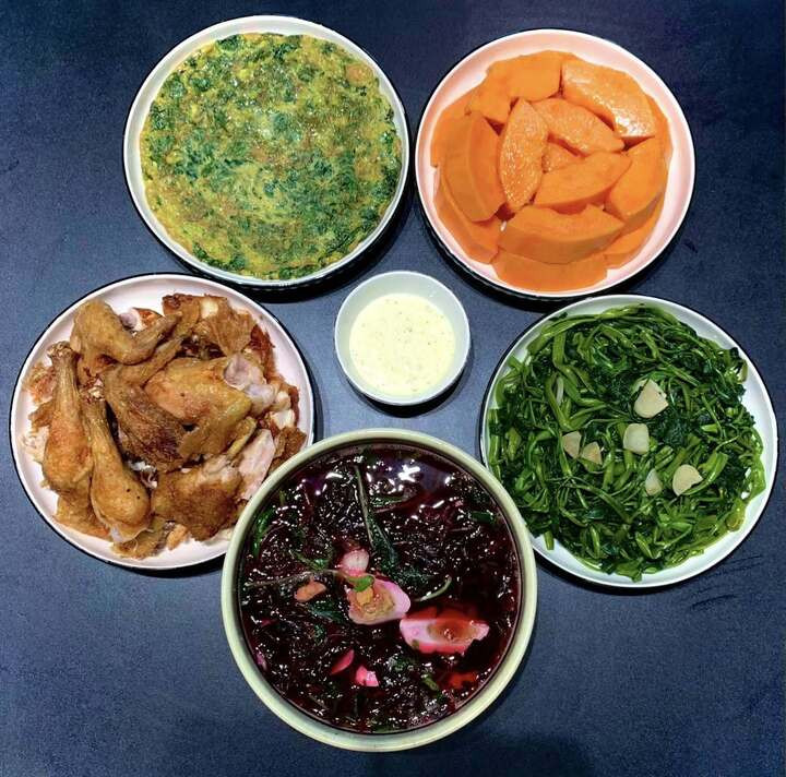 Mâm cơm đơn giản với gà chiên, trứng rán, rau xào, canh rau dền và tráng miệng bằng đu đủ.