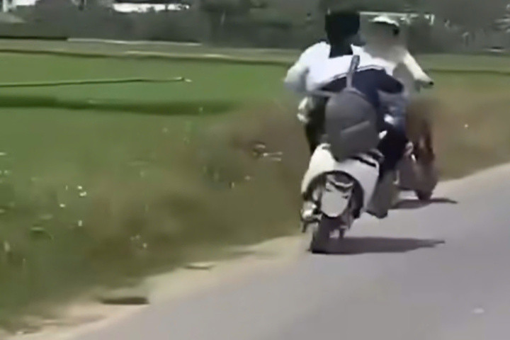Hai thiếu niên điều khiển xe điện lạng lách, đánh võng trên một đoạn đường dài, bất ngờ tạt đầu rồi mất lái, trượt ngã và va chạm với người phụ nữ đang dừng xe bên đường. (Ảnh cắt từ clip)