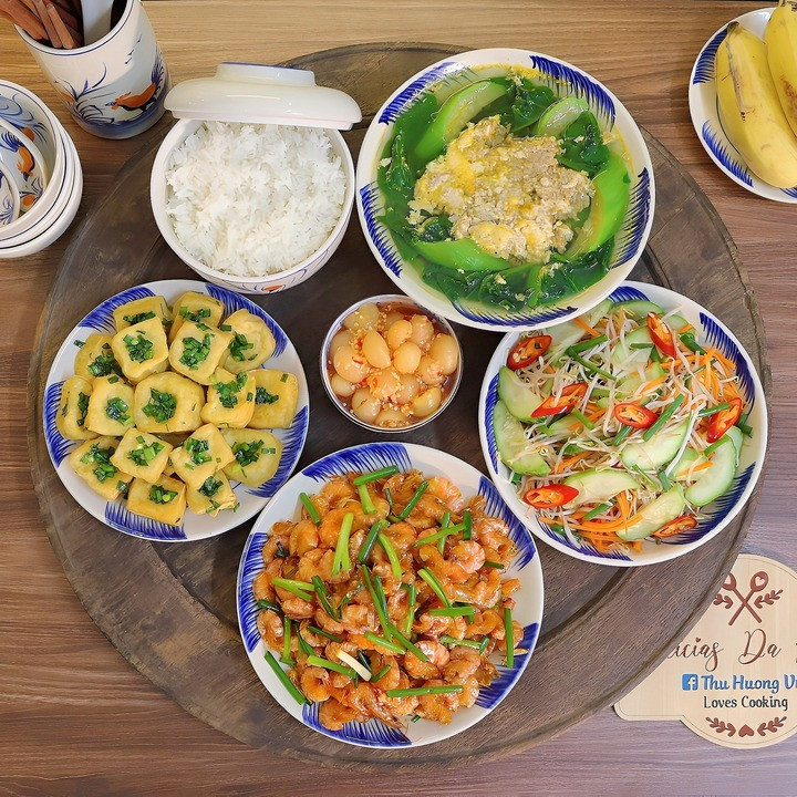 Mâm cơm có món tôm vằn biển rang, đậu phụ rán tẩm hành, canh cua nấu rau mồng tơi mướp, dưa chuột trộn giá đỗ.