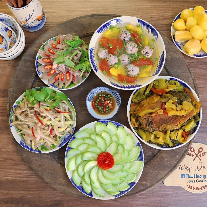 Mâm cơm có món cá trắm kho dưa, chạo tai heo xoài xanh bóp thấu, lưỡi heo luộc, canh chua mọc nấu dứa, dưa chuột mèo.