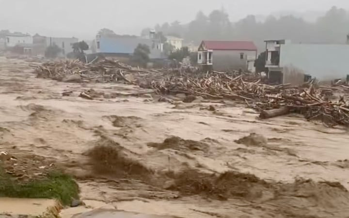 Nước lũ dâng cao tràn qua Quốc lộ 32, khiến các phương tiện tạm thời không thể đi lại, một số hộ dân bị nước lũ cô lập. (Ảnh chụp màn hình)