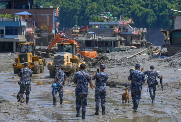 Cảnh sát Nepal quan sát khi máy xúc dọn dẹp đống đổ nát sau trận lũ quét. (Ảnh: AP)