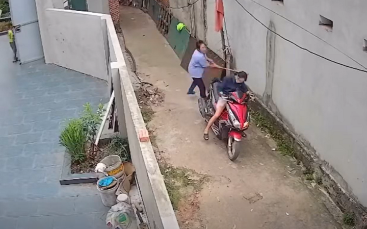 Người phụ nữ áo xanh cầm chổi đập mạnh vào đầu hàng xóm. (Ảnh cắt từ clip)